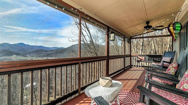 Une véranda couverte offrant une vue sur les montagnes, avec une balustrade en bois et du mobilier d’extérieur.