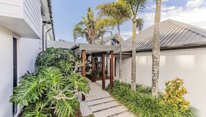A modern house with a covered patio, surrounded by lush tropical plants and palm trees. - Santi House (Kingscliff)