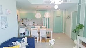 A modern kitchen with white cabinets, a dining area with white chairs, and a blue sofa with patterned cushions.