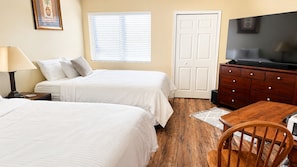 A hotel room with two beds, a TV, a wooden dresser, and a desk with a chair.