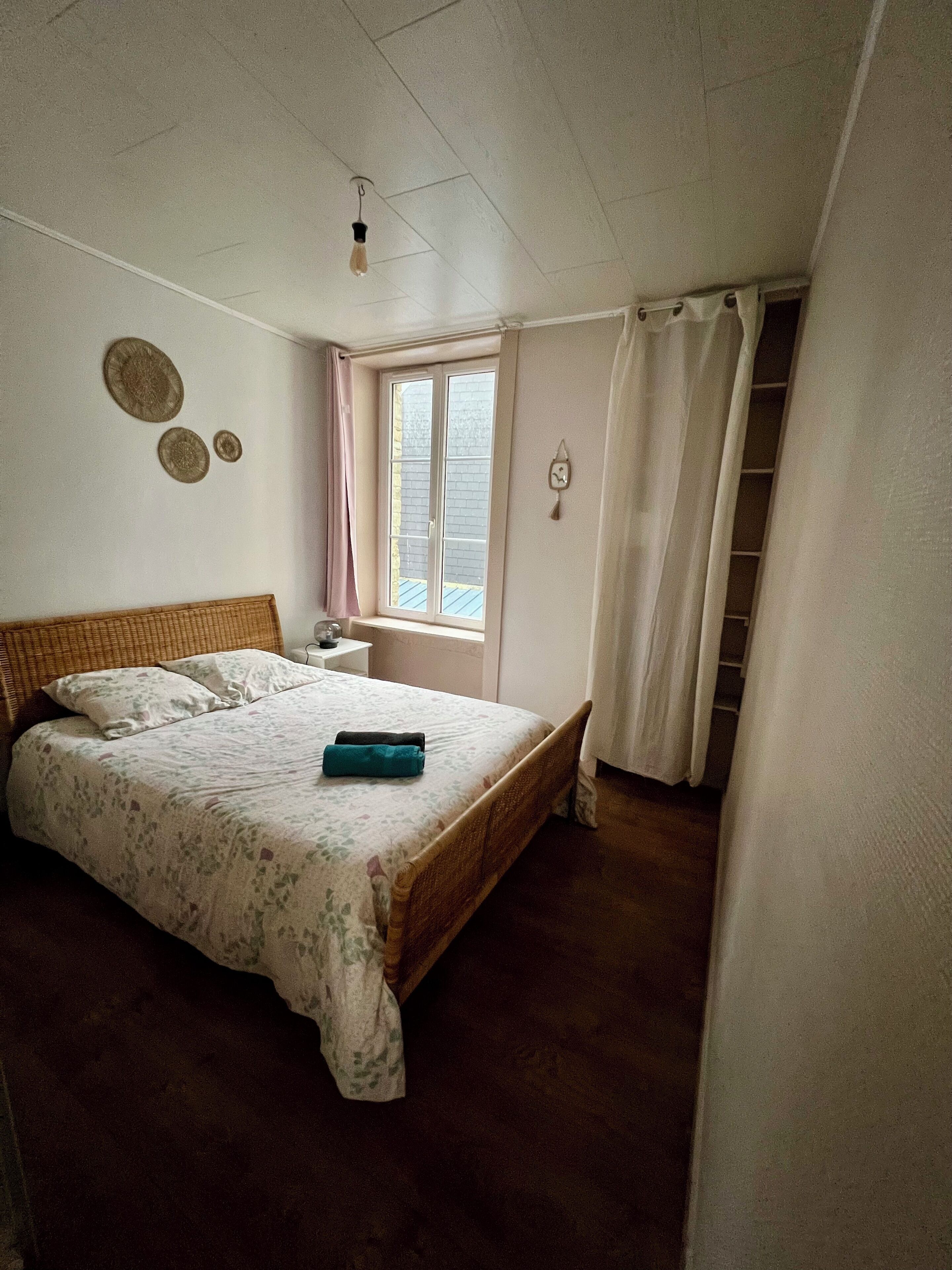 A bedroom with a bed, a window, a bedside table, and a wardrobe.
