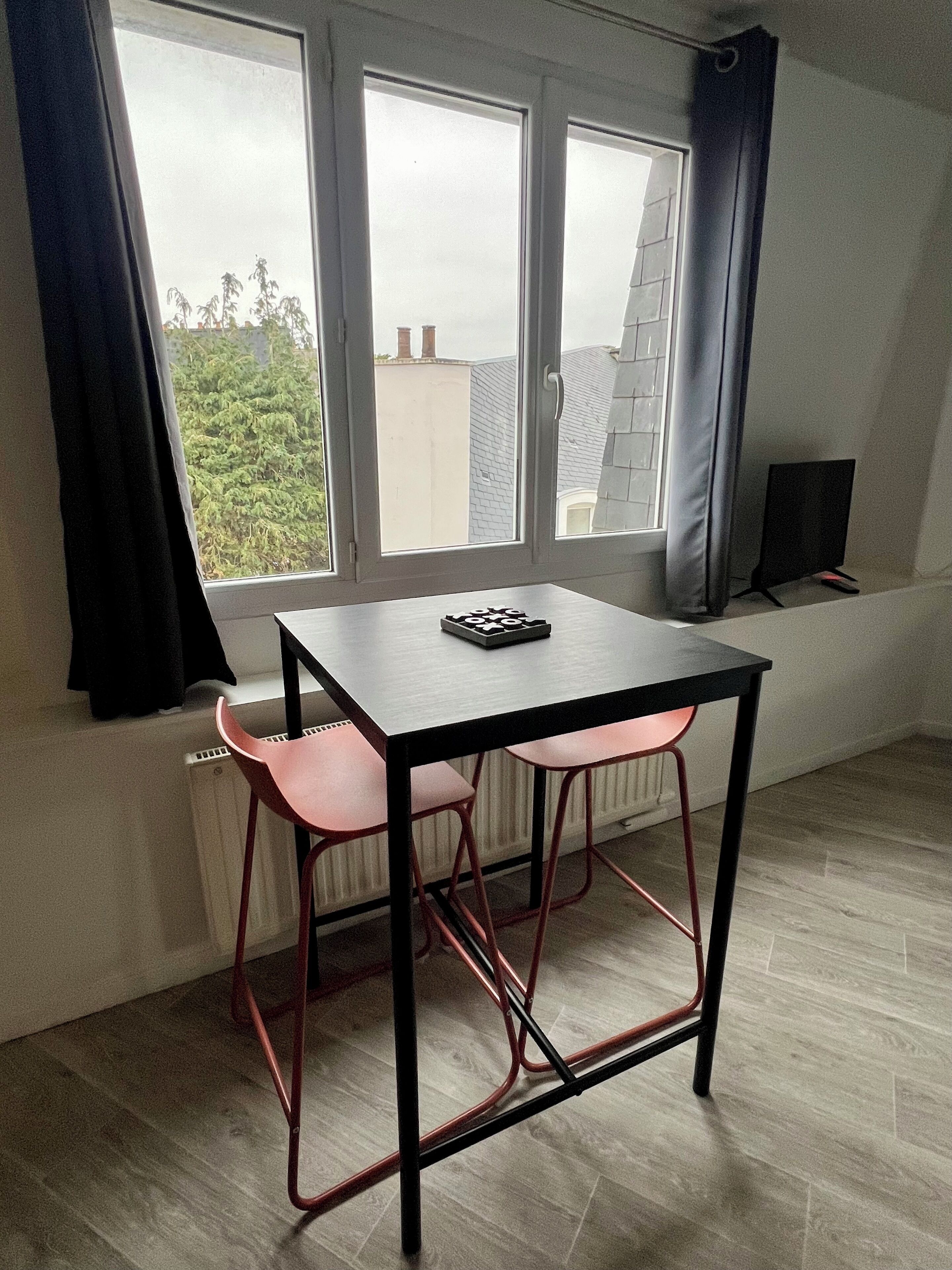 A small room with a table and two chairs, a window with curtains, and a radiator.