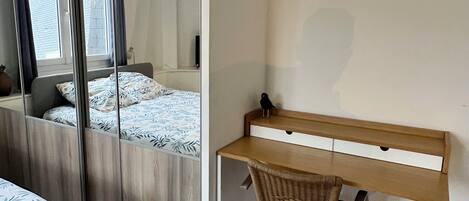 Un dormitorio con cama, escritorio, silla y un espejo grande.