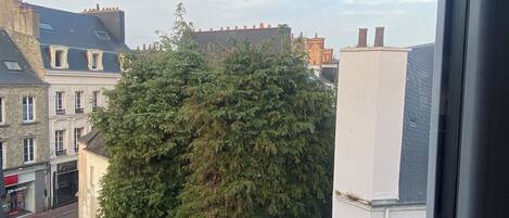 Vista de la calle con edificios, un árbol y cielo despejado.