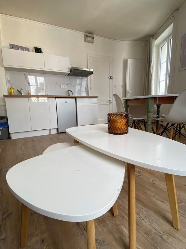 Una cocina moderna con armarios blancos, horno empotrado y campana extractora de acero inoxidable. Hay una mesa de comedor blanca con patas de madera y un jarrón decorativo.