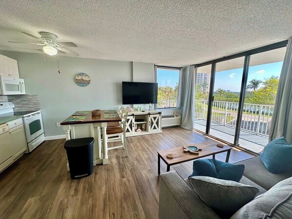 A living room with a dining area, a TV, and a balcony with a view.