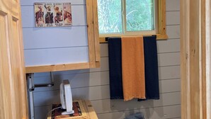 Pieni, viihtyisä huone, jossa on puinen katto, ikkuna, josta avautuu näkymä puihin, pieni lämmitin ja puinen kaappi.