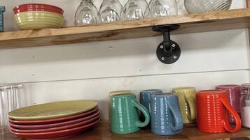 A kitchen shelf with stacked plates, glassware, and colorful mugs.