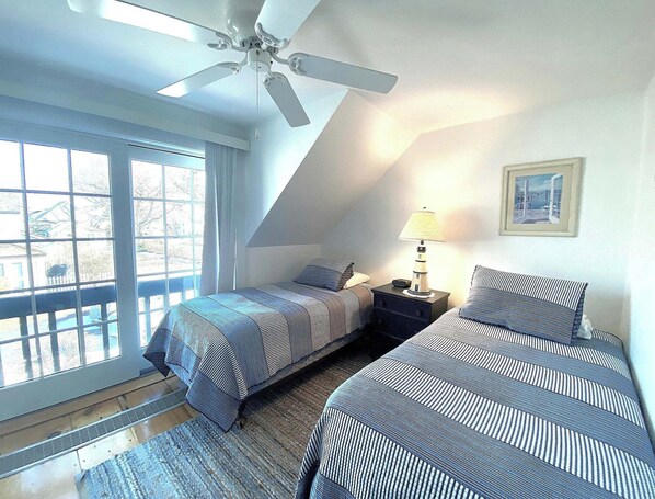 A bedroom with two beds, a ceiling fan, a nightstand with a lamp, and a window with a view. - Maushop Village, 2-bedroom, 1.5 baths, Sleeps 4, A/C, patios & private beach (Mashpee)