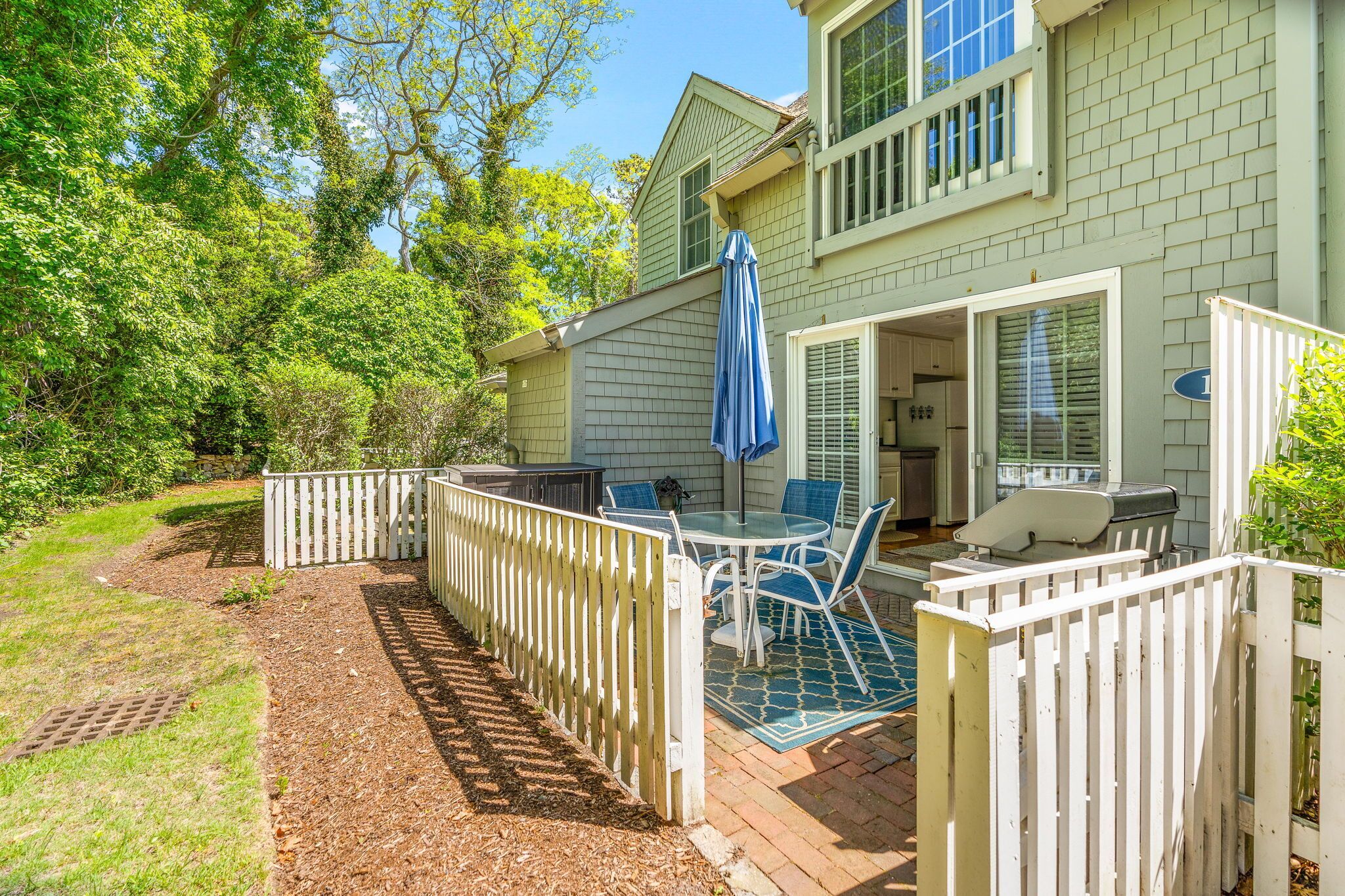 A patio with a table and chairs, a white fence, and a house with a garage.