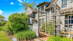 A two-story house with a white fence, a number 17 sign, and a brick pathway. - Maushop Village, 2-bedroom, 1.5 baths, Sleeps 4, A/C, patios & private beach (Mashpee)