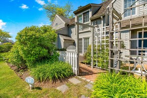 A two-story house with a white fence, a number 17 sign, and a brick pathway. - Maushop Village, 2-bedroom, 1.5 baths, Sleeps 4, A/C, patios & private beach (Mashpee)