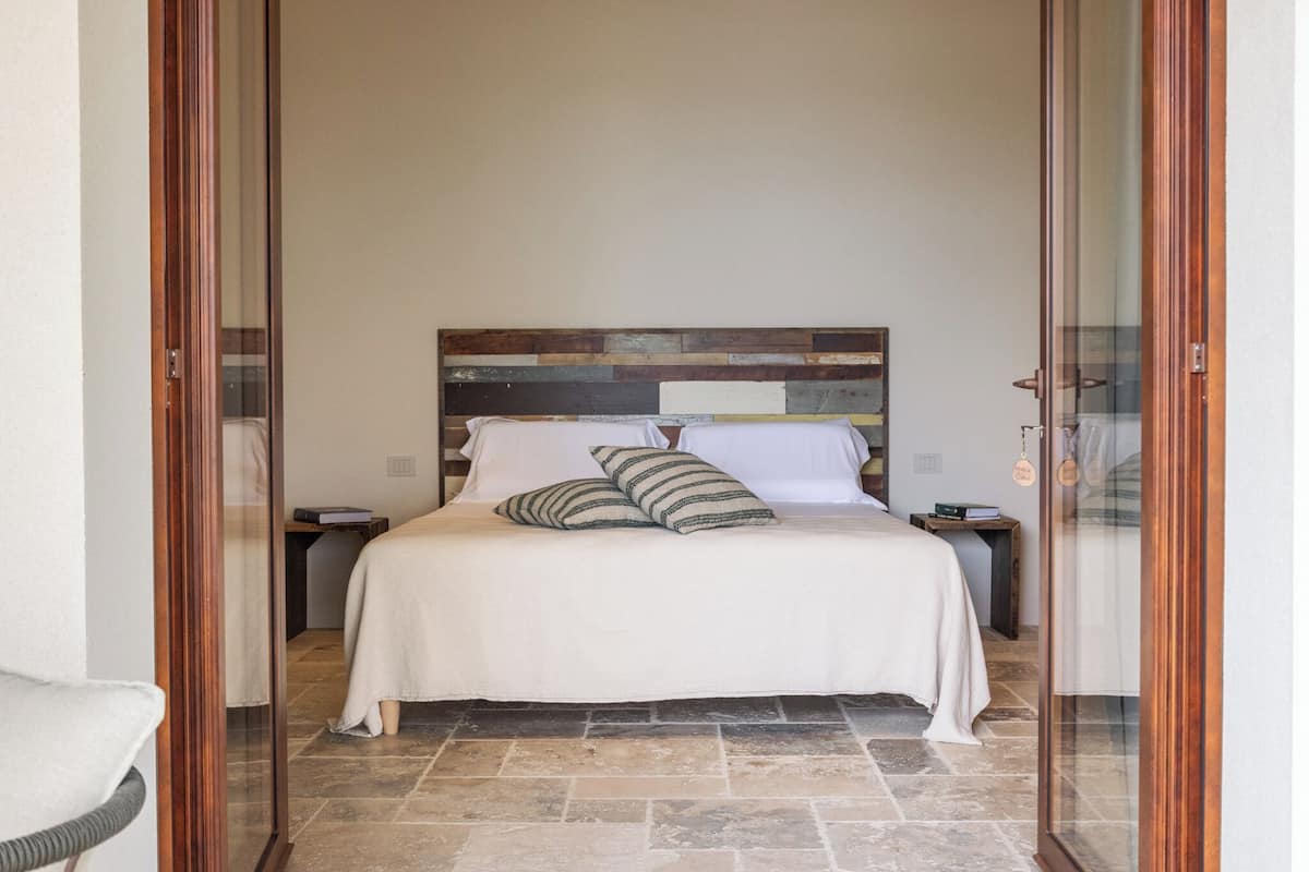 A bedroom with a wooden headboard, a white bedspread, and striped pillows.