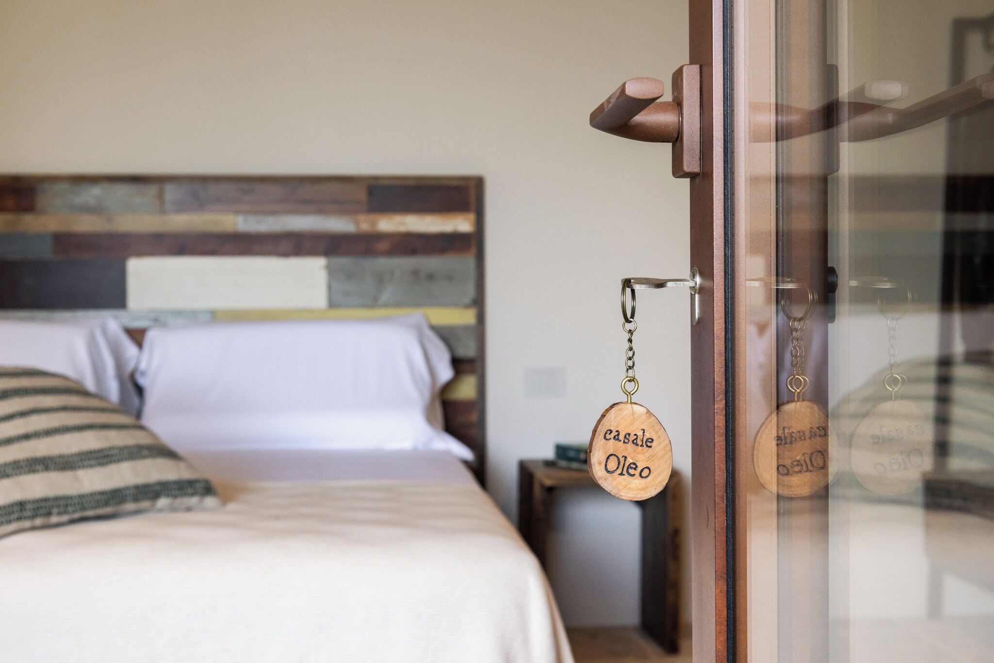 Quarto com cama, cabeceira de madeira e porta de madeira com um chaveiro pendurado.