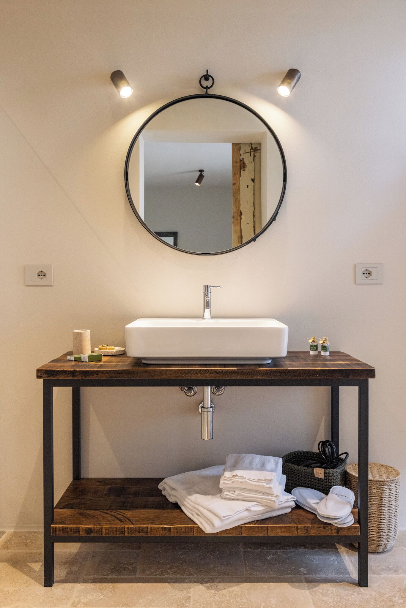 A bathroom with a white sink, wooden vanity, and a round mirror with lights.