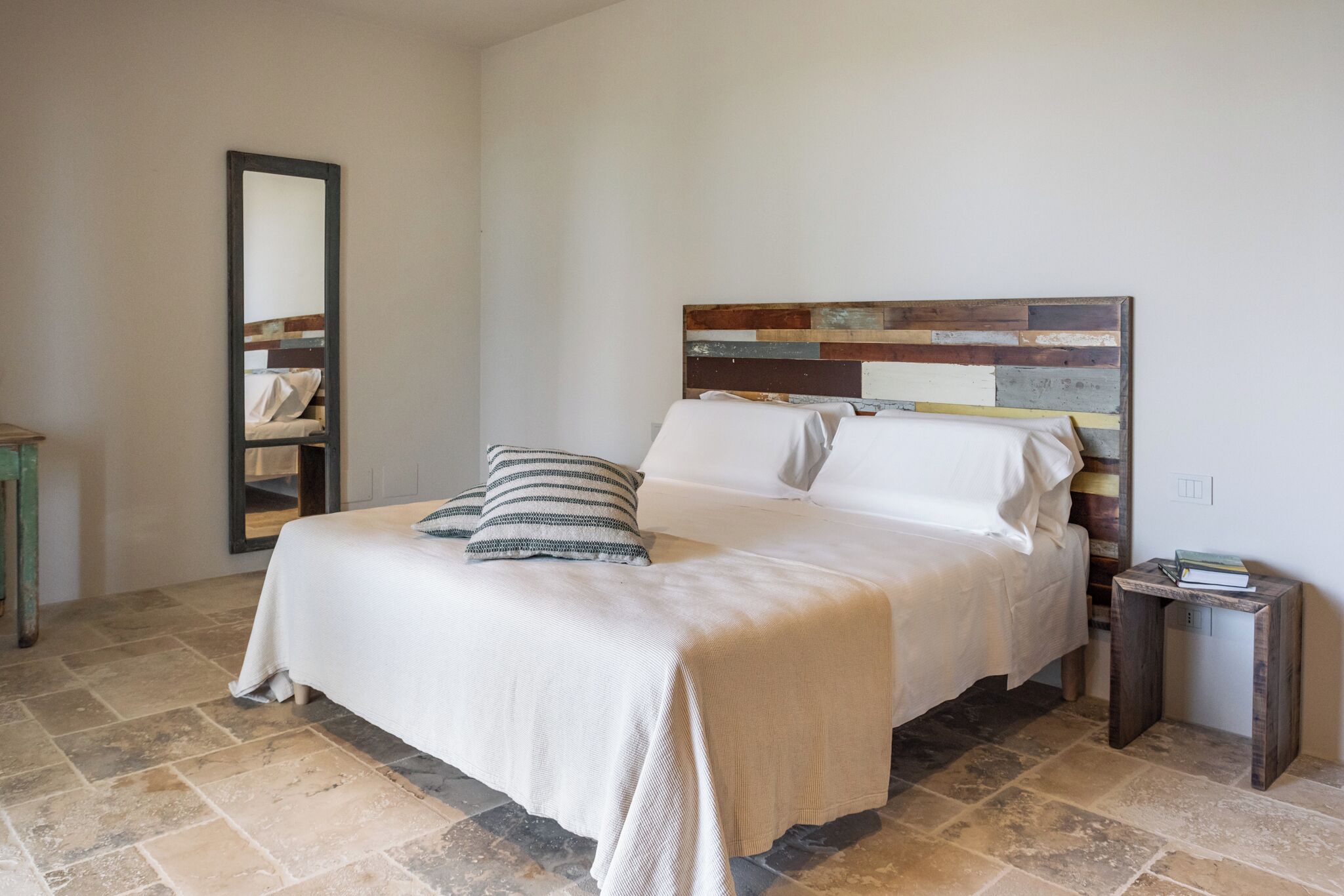 Un dormitorio con una cama grande, cabecera de madera, mesita de noche y espejo.