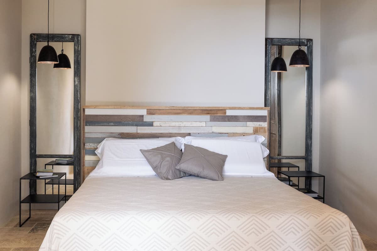 A neatly made bed with a patterned bedspread, two pillows, and a headboard with a wooden and metal design. There are two bedside tables with lamps on either side of the bed.