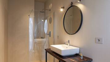 Un baño moderno con ducha de vidrio, un lavamanos blanco y un espejo redondo en la pared.