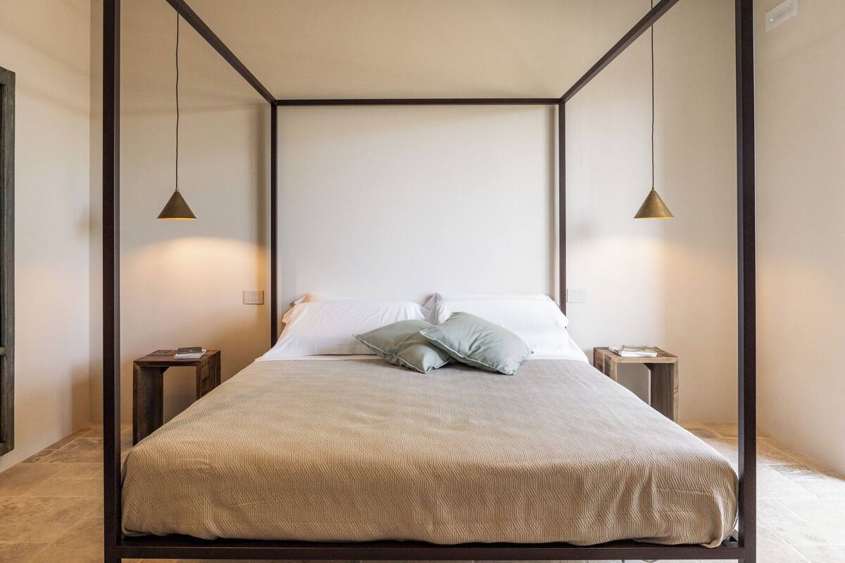 A modern bedroom with a four-poster bed, two bedside tables, and pendant lighting.