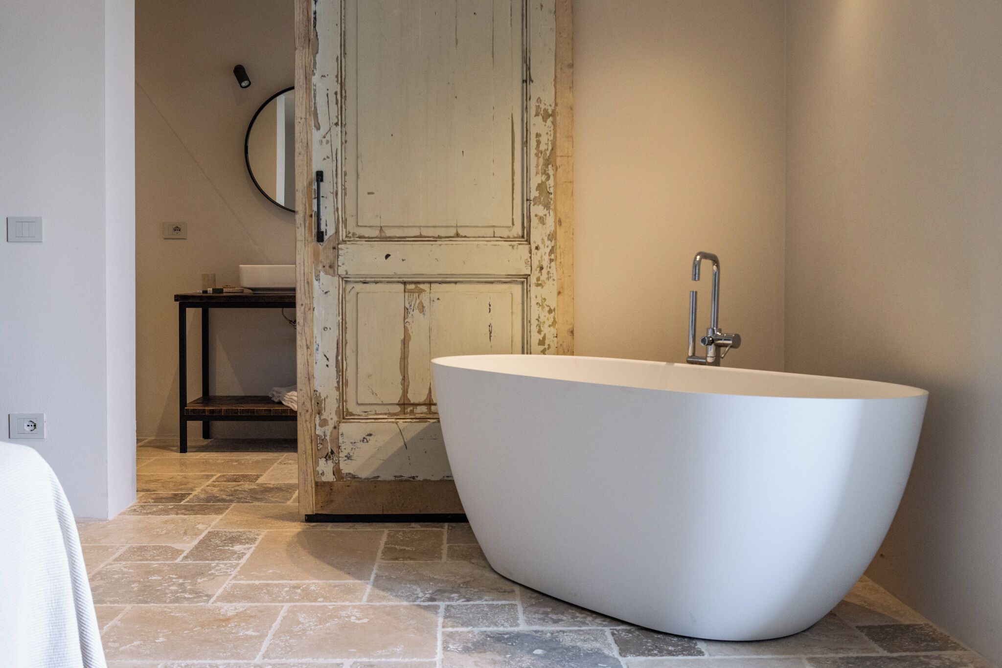 A modern bathroom with a freestanding bathtub, a wooden door, and a small table with a mirror.