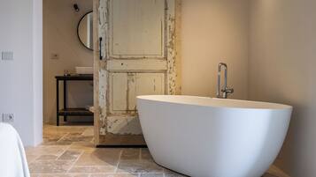 A modern bathroom with a freestanding bathtub, a wooden door, and a small table with a mirror.