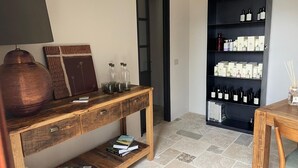 A room with a wooden console table, a lamp, books, and a black shelving unit with bottles.