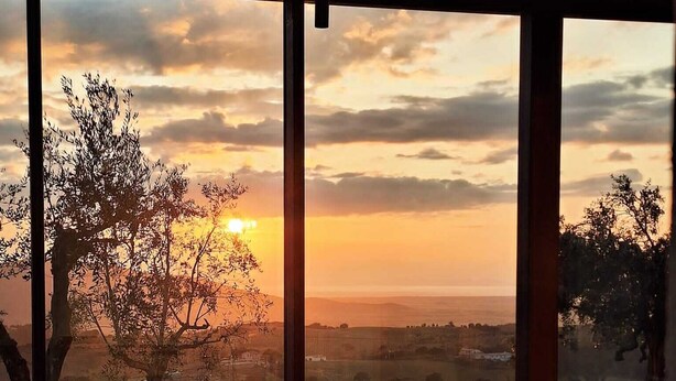 A dining area with a table set for four, large windows offering a view of the sunset over a landscape.