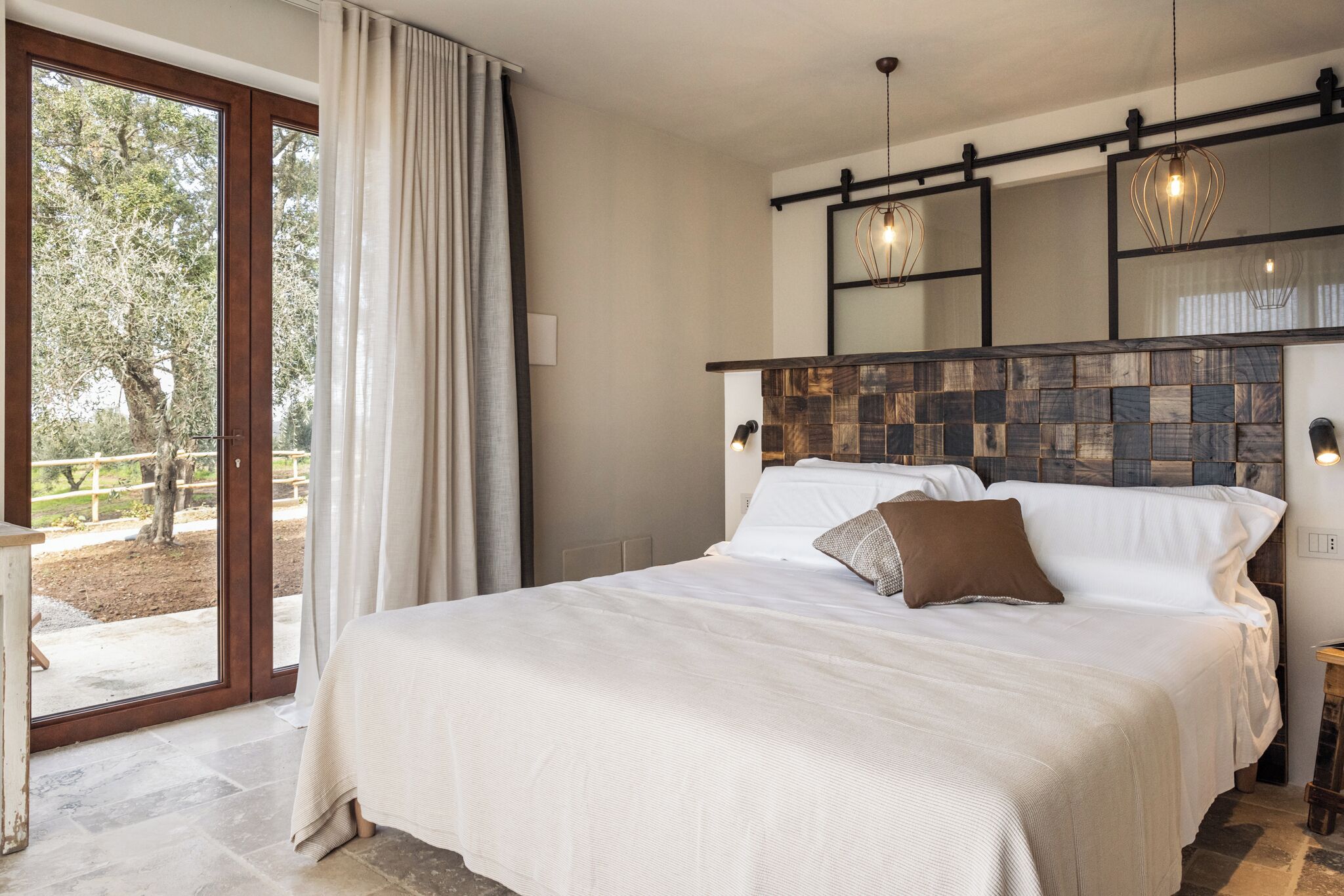 Een slaapkamer met een groot bed, een houten hoofdeinde en een schuifglazen deur die uitkomt op een terras.