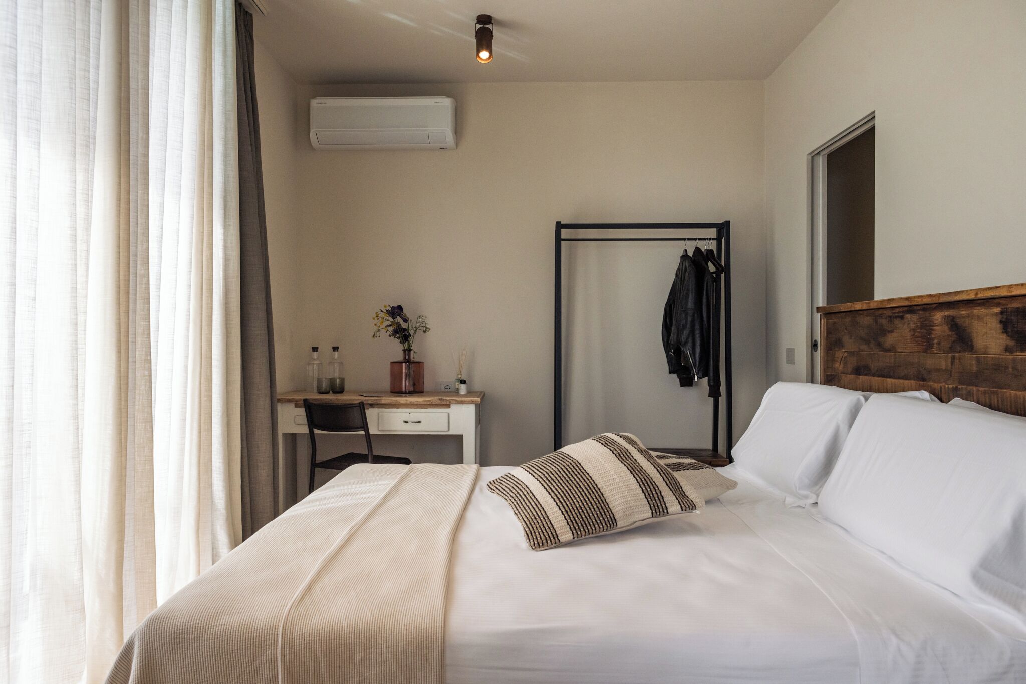 A hotel room with a bed, a desk, a chair, a mirror, and a wardrobe.