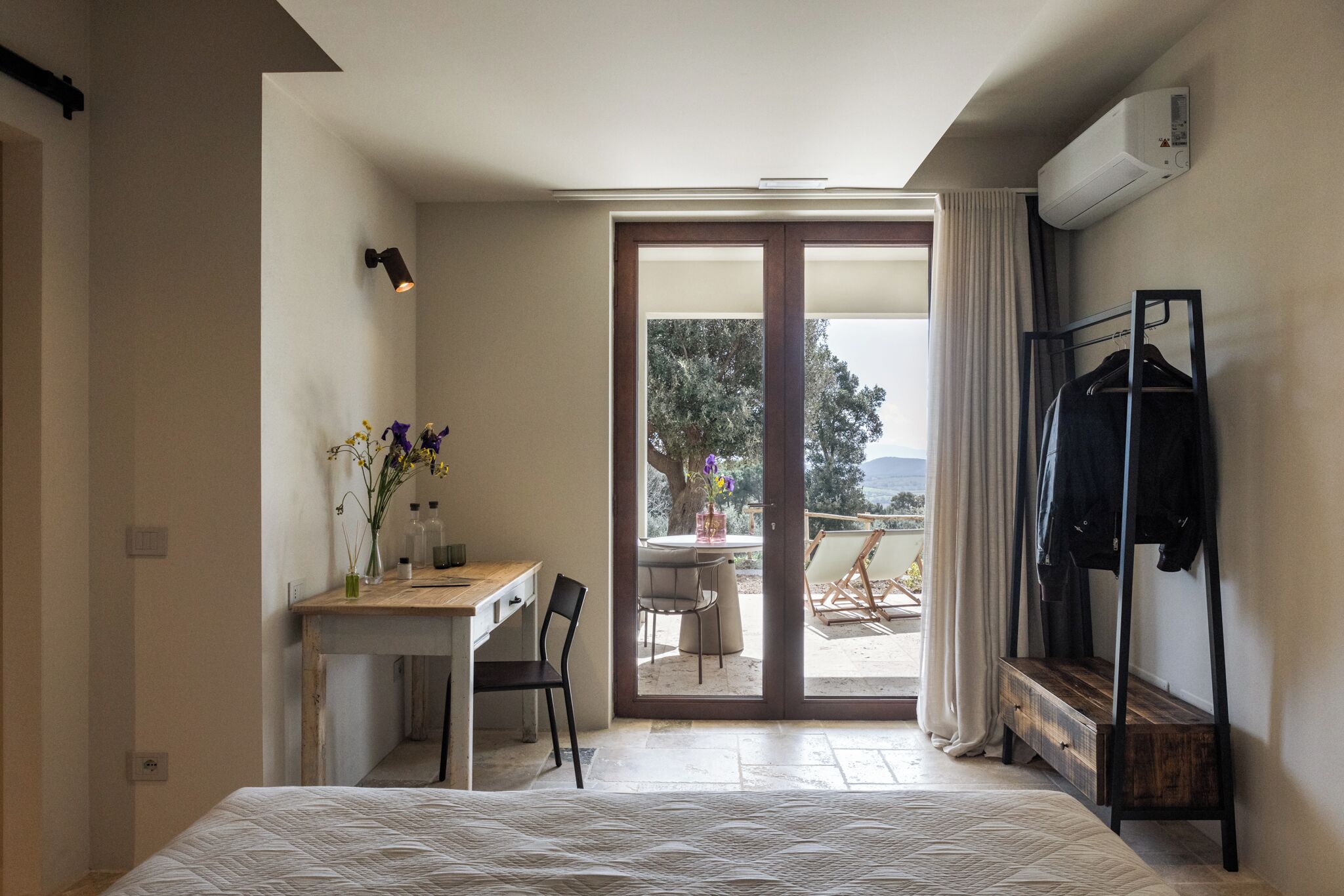 Un dormitorio con cama, escritorio, silla, mesa y vistas a un espacio exterior con mesa y sillas a través de una puerta corrediza.