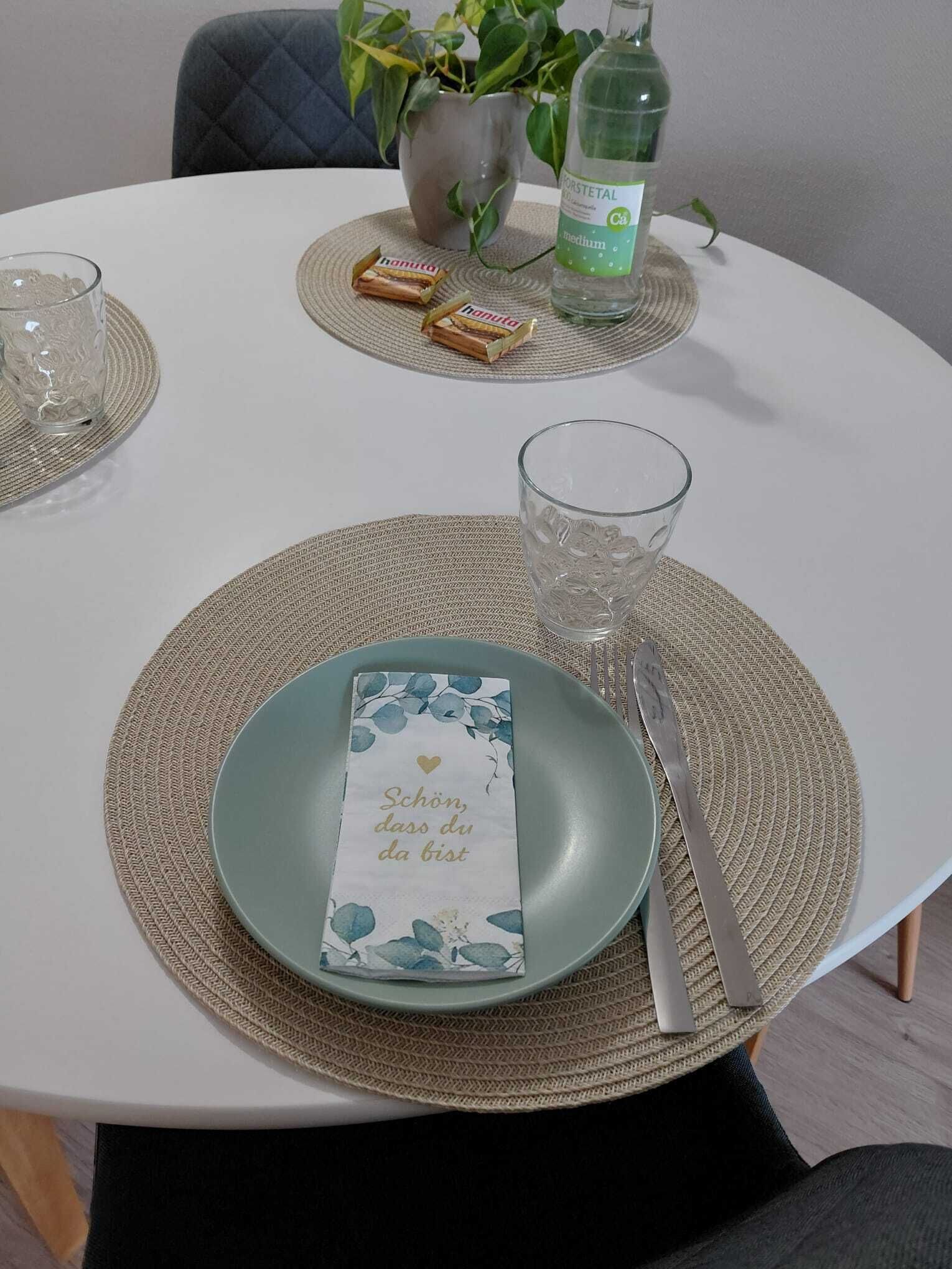 Una mesa dispuesta con un mantel individual, un plato, una servilleta, un vaso y una botella de agua.