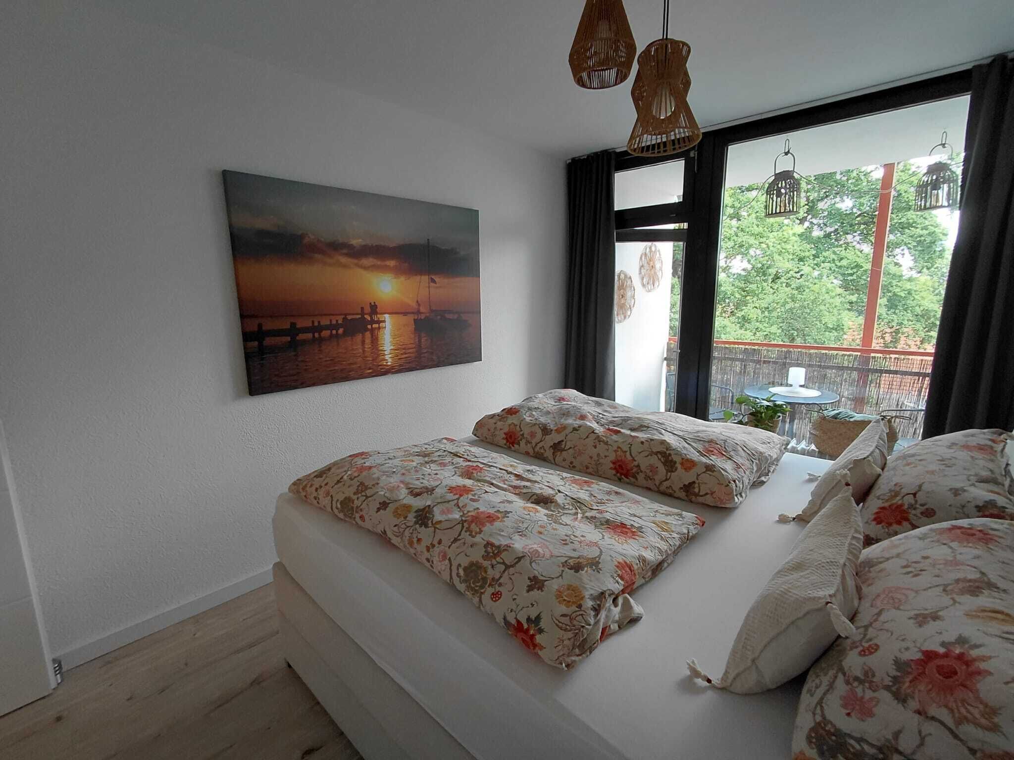 Quarto com cama, pintura de um pôr do sol e vista para o verde pela janela.