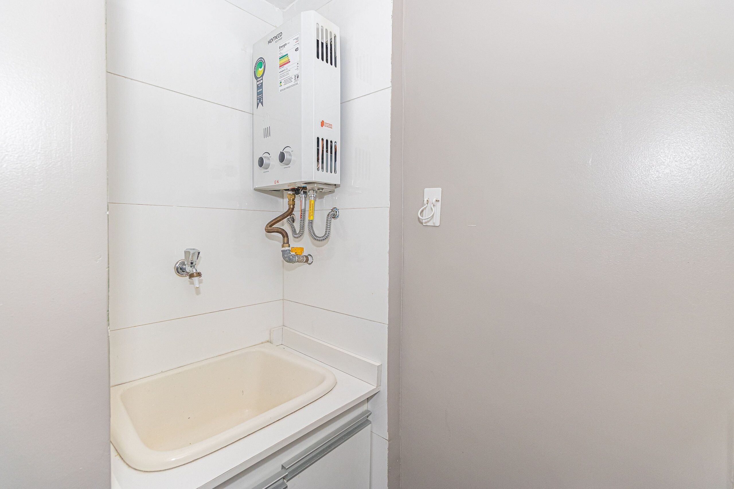 Un baño con pared de azulejos blancos, un lavamanos blanco y un calentador de agua montado encima.
