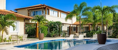 A pool area with lounge chairs and a building with a tiled roof.