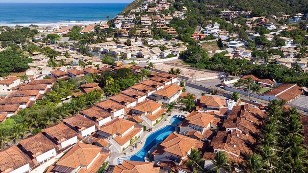 Zona residencial costera con casas de techos de teja terracota, una piscina central y vista al océano.