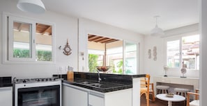 Eine moderne Küche mit Herd, Spüle und viel Arbeitsfläche. Zwei Fenster sorgen für natürliches Licht und bieten Blick ins Grüne.