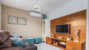 Una sala de estar moderna con un sofá de cuero marrón, otomanas color turquesa, un mueble de madera para entretenimiento con televisor de pantalla plana y papel tapiz a rayas.
