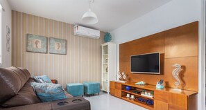 Ein modernes Wohnzimmer mit einem braunen Ledersofa, Türkis-farbenen Hocker, einer Holz-Unterhaltungsecke mit Flachbildfernseher und gestreifter Tapete.