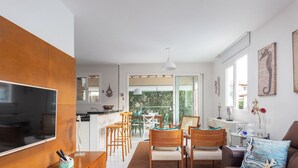 Una sala de estar moderna con televisor, sillas de madera, un sofá y un comedor con mesa y sillas.