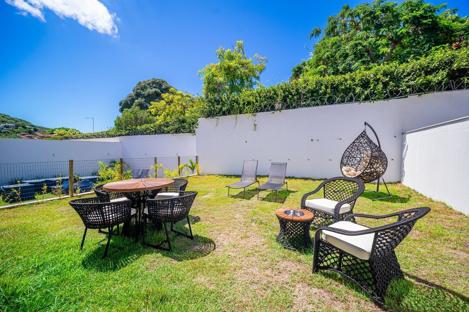 Une terrasse avec une table ronde et des chaises, un fauteuil suspendu et une petite table ronde.