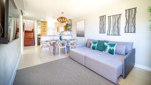 Ein modernes Wohnzimmer mit grauem Sofa, einem Esstisch mit Stühlen und einer Küche im Hintergrund.