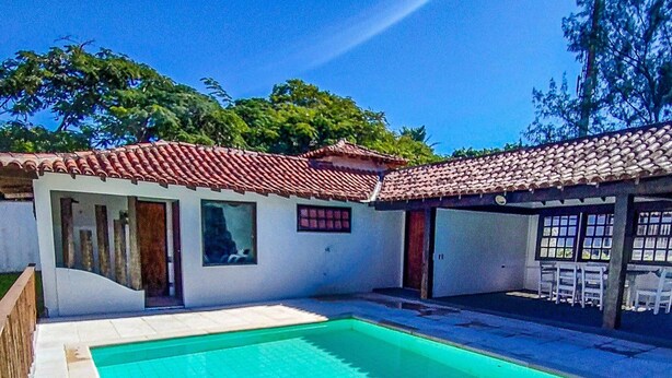 A swimming pool with tiled flooring, a building with a tiled roof, and a clear blue sky. - Bz39 House with private pool 300m from the beach! (Armação dos Búzios)