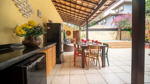 A covered outdoor kitchen area with a dining table and chairs, a refrigerator, and a decorative fish wall art piece.