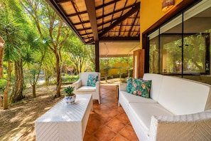 An outdoor patio with wicker furniture, a potted plant, and a view of the surrounding greenery. - Center 600m from Rua das Pedras! House with 5 suites Bz86 (Armação dos Búzios)