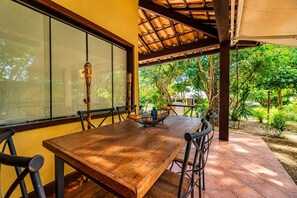 A wooden table with chairs, a glass partition, and a view of greenery outside.