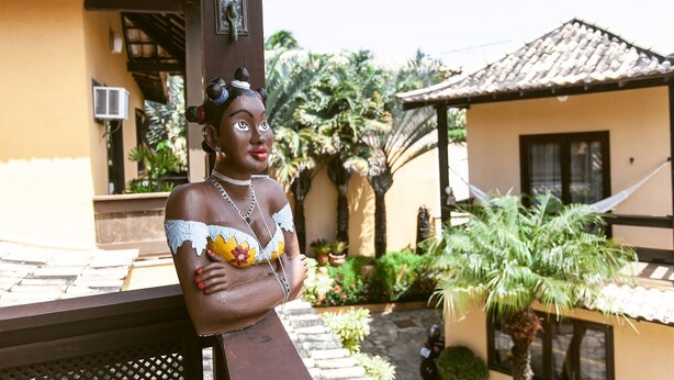 Une statue représentant une femme, dans un décor tropical, avec un toit recouvert de tuiles et des palmiers.