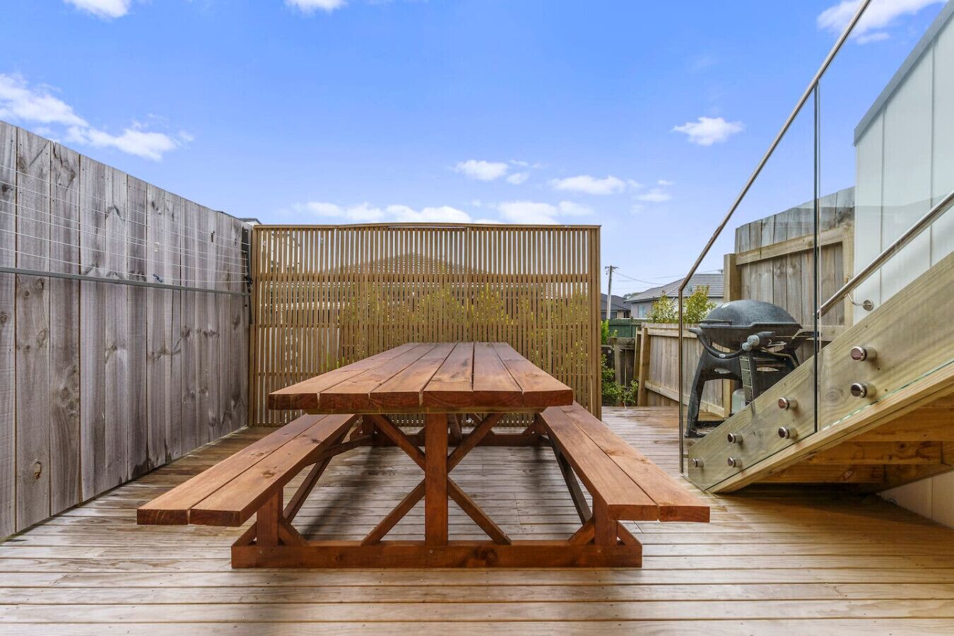 A wooden deck with a picnic table and benches, surrounded by wooden fences and a glass railing.