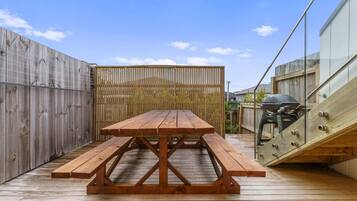 A wooden deck with a picnic table and benches, surrounded by wooden fences and a glass railing.