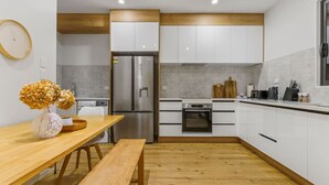 A modern kitchen with white cabinets, stainless steel appliances, and a wooden dining table with a bench. - Modern Orewa Delight w Parking just Steps to Beach (Auckland Hibiscus Coast)