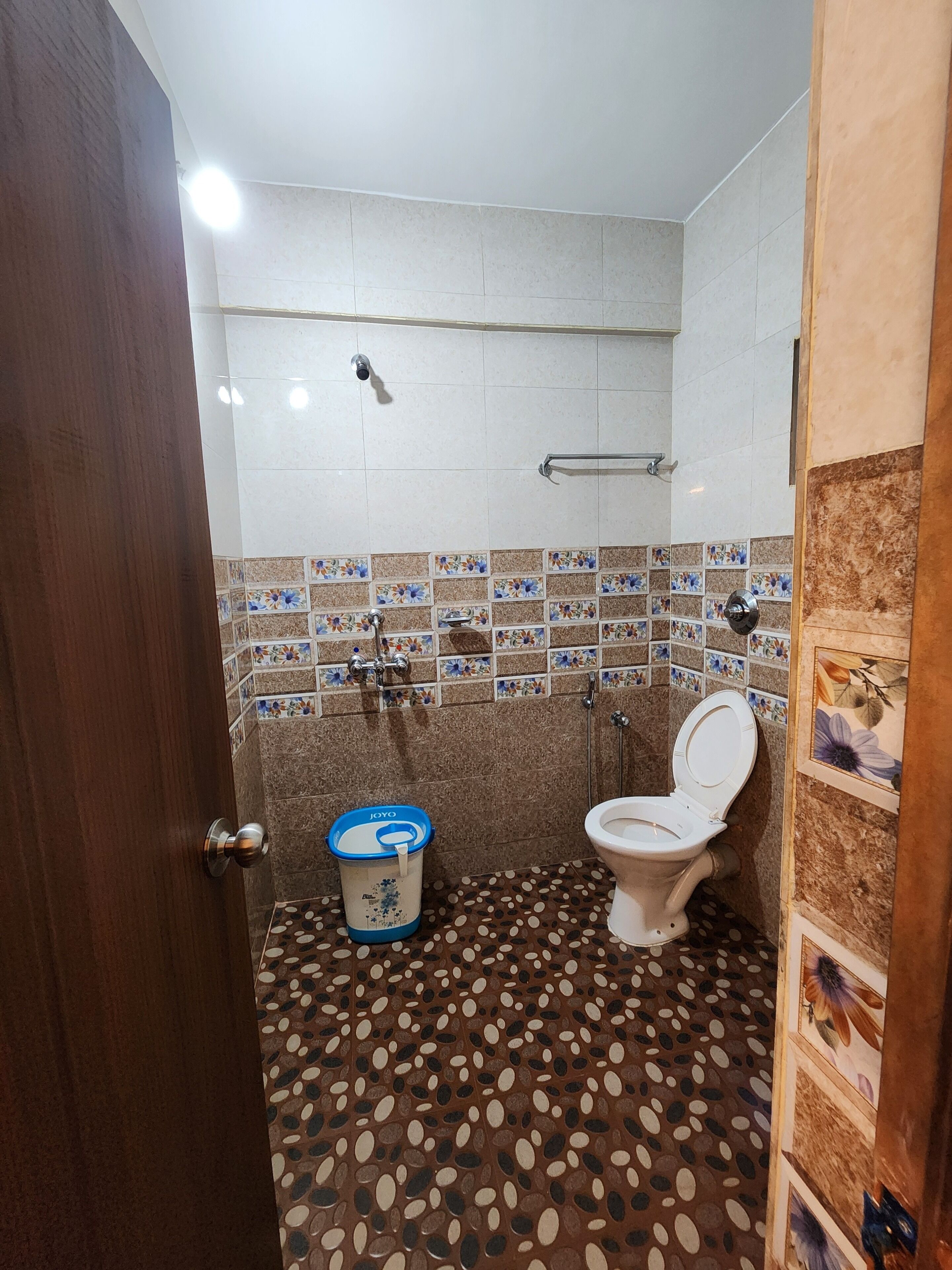 Un bagno con il water, una doccia e un lavandino. Il pavimento presenta un motivo a pois, e le pareti sono rivestite di piastrelle con motivi floreali.